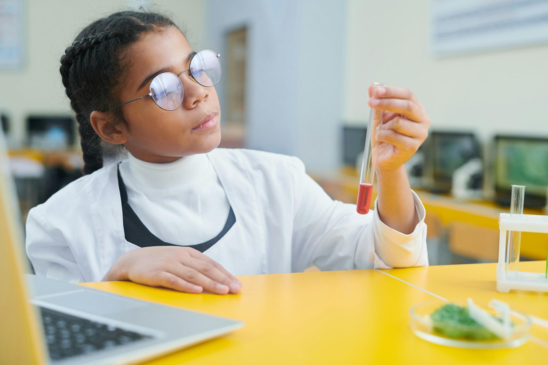 Une petite fille avec une blouse scientifique qui regarde un flacon